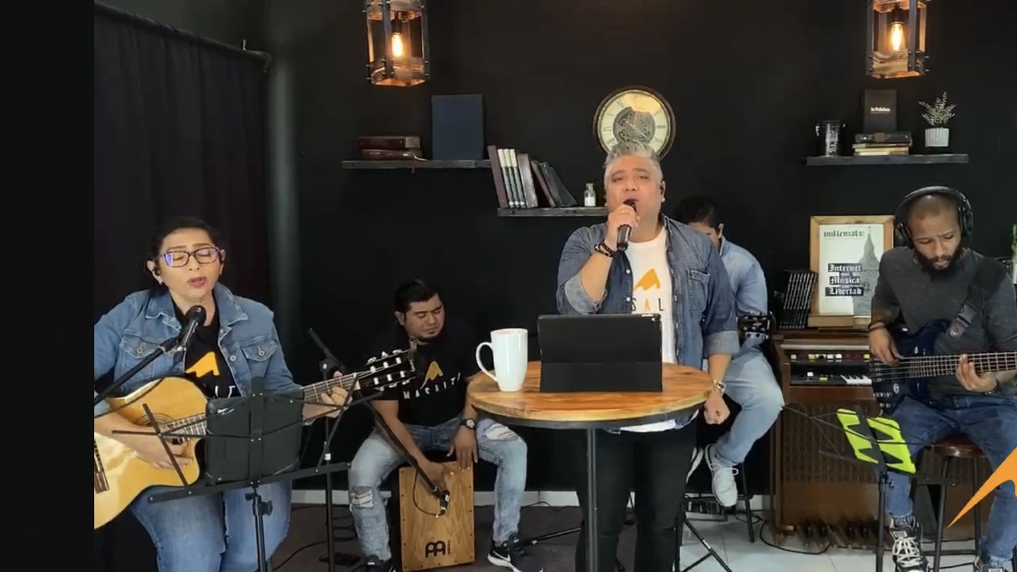 La banda de la comunidad tocando en la sala de una casa pintada de negro, convertida en escenario para transmitir